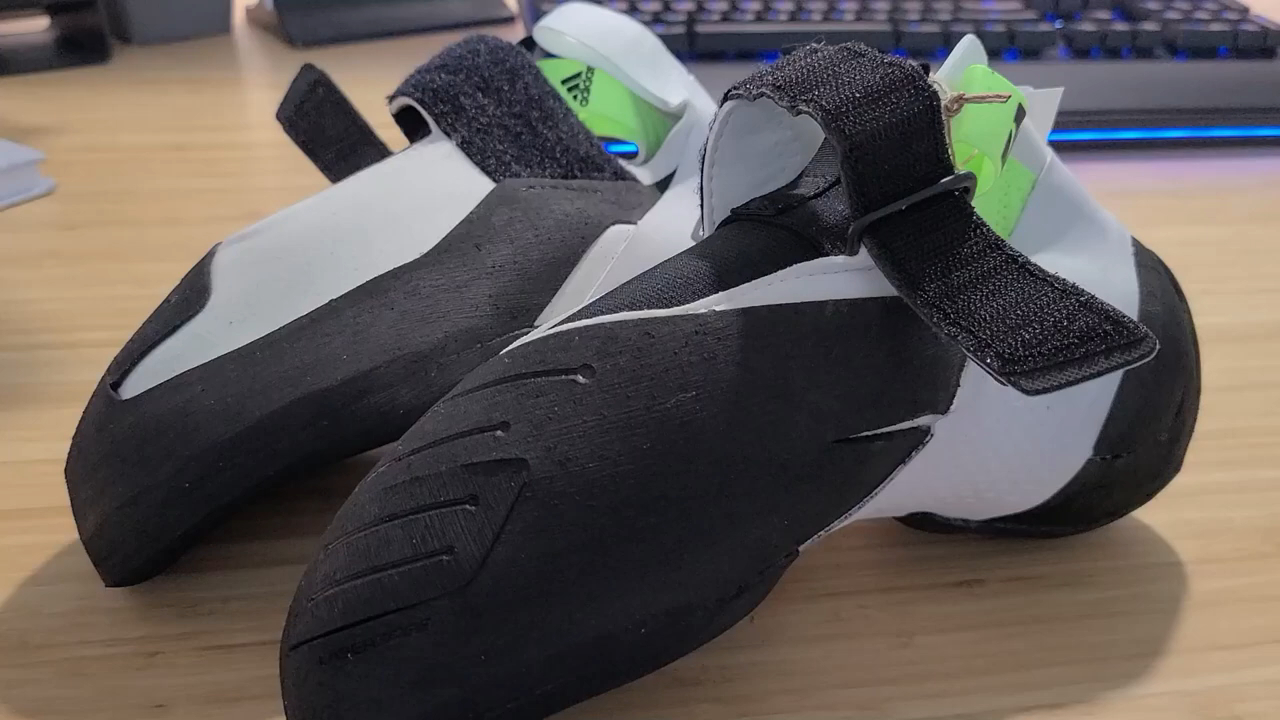 close-up of Five Ten Hiangle climbing shoes placed on a wooden desk, featuring their unique black and white design with Velcro straps