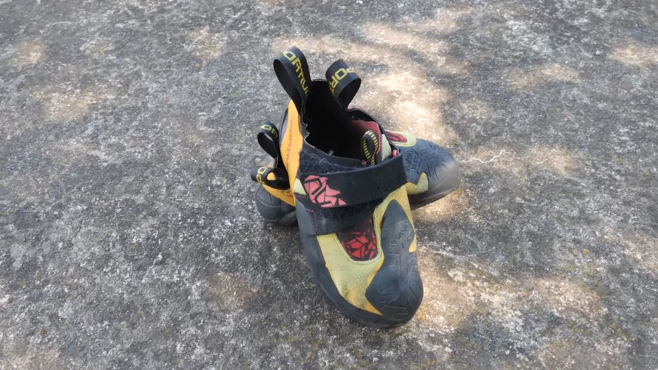 pair of La Sportiva Skwama climbing shoes with a yellow and black design, placed on a concrete surface under dappled sunlight