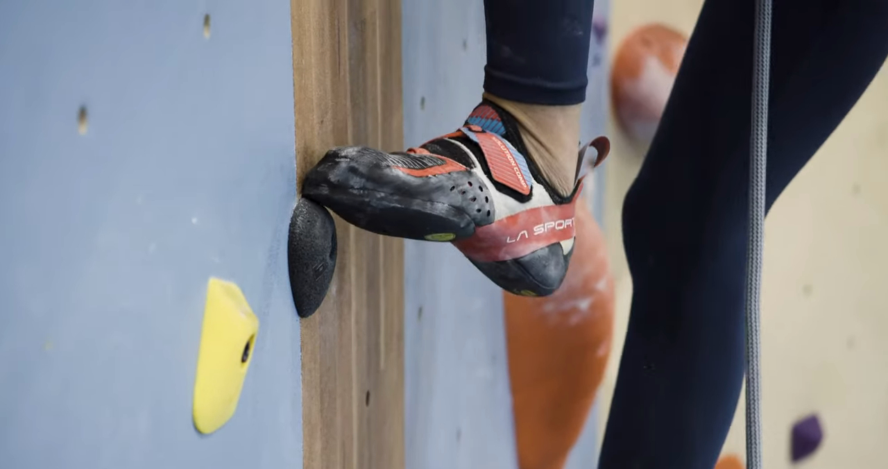 Close-up of a climber’s foot wearing La Sportiva Solution Comp climbing shoes on an indoor climbing hold