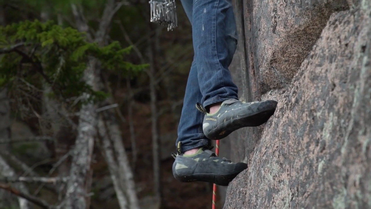 climber's feet in La Sportiva Tarantula climbing shoes, gripping a rock face in a forested area