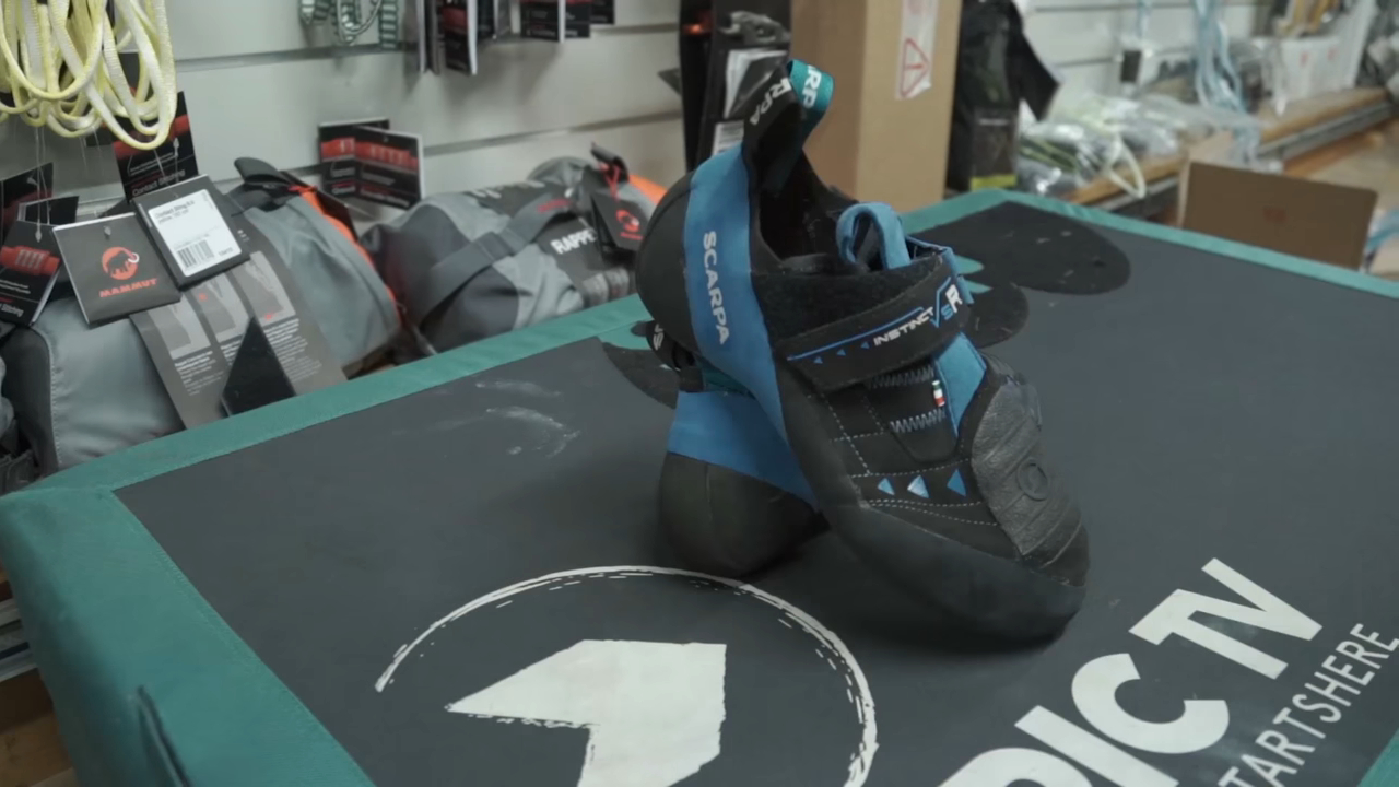 pair of Scarpa Instinct VS-R climbing shoes in blue and black displayed on a green table in a climbing gear shop