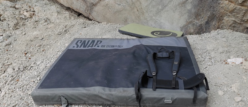 Two bouldering pads resting at the base of a climbing crag