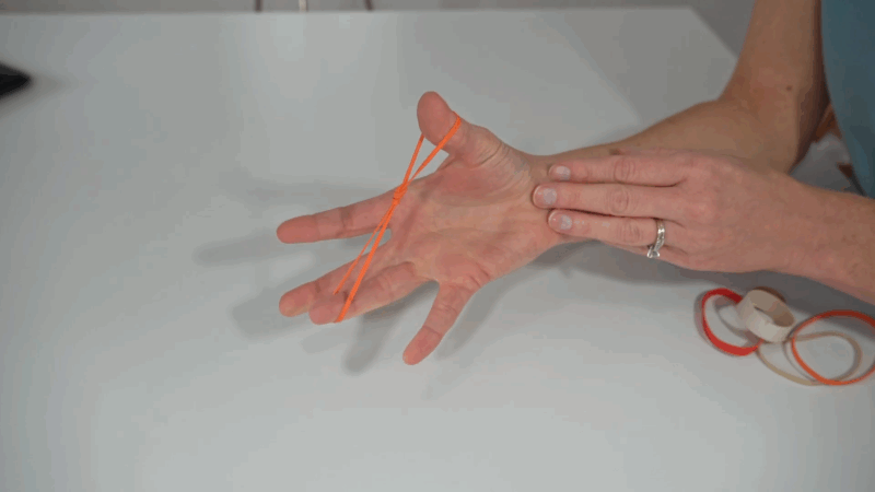 A person uses a small rubber band for a finger extension exercise to improve grip balance and strength