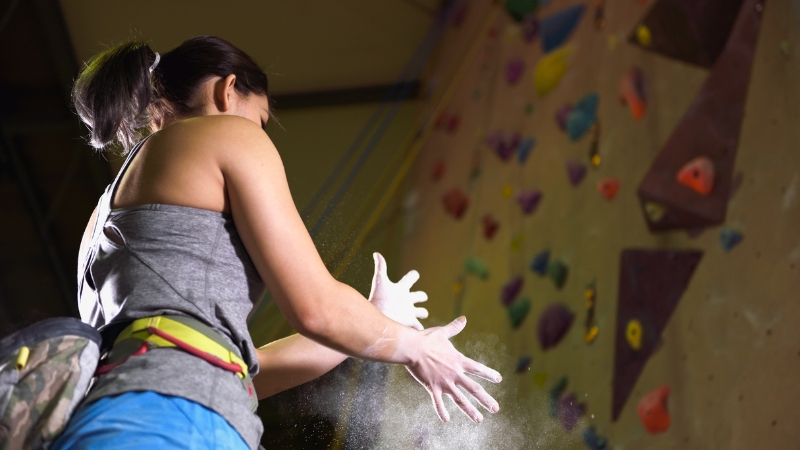 A climber prepares for a bouldering session by chalking up hands to improve grip strength and control
