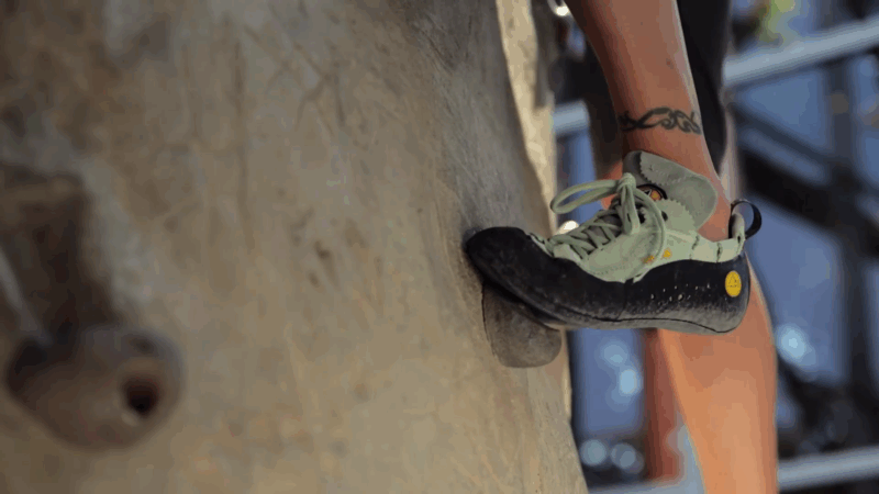 A climber’s foot presses onto a small foothold with worn bouldering shoes during an indoor climbing session