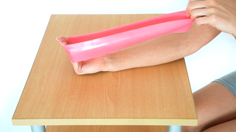 A person uses a resistance band on a flat surface to strengthen wrist and forearm muscles for better grip strength
