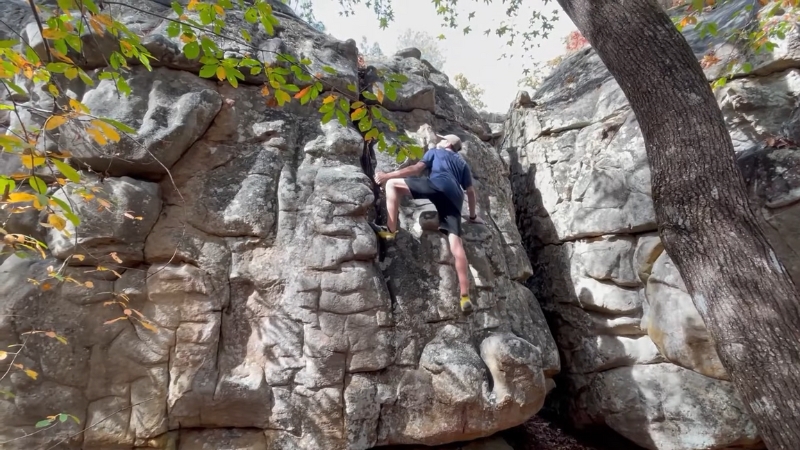 A climber scales a sandstone boulder at Horse Pens 40 in Alabama on a clear day