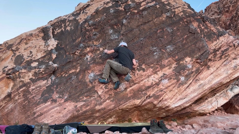A climber moves across a low sandstone boulder at the Kraft Boulders in Nevada with crash pads below