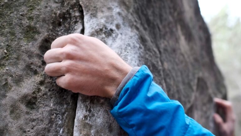 A climber grips a rock hold during an outdoor bouldering session on a beginner-friendly route