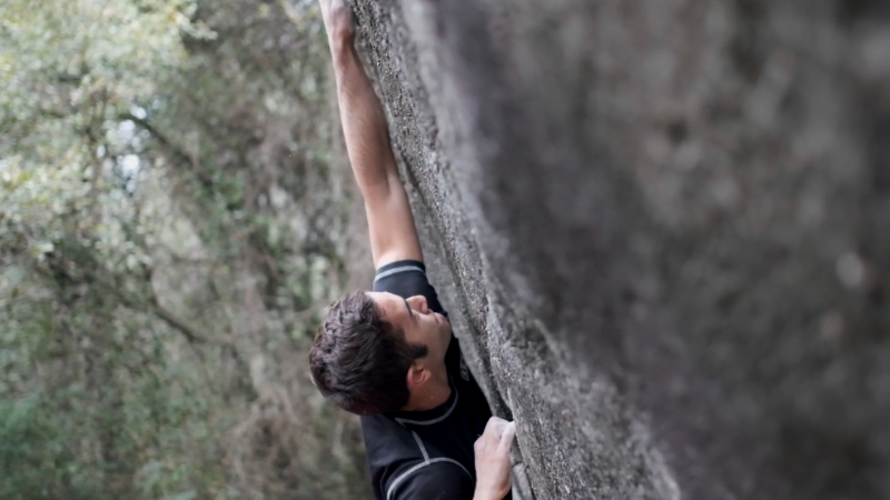 A beginner climbs a rock wall outside, reaching for the next hold